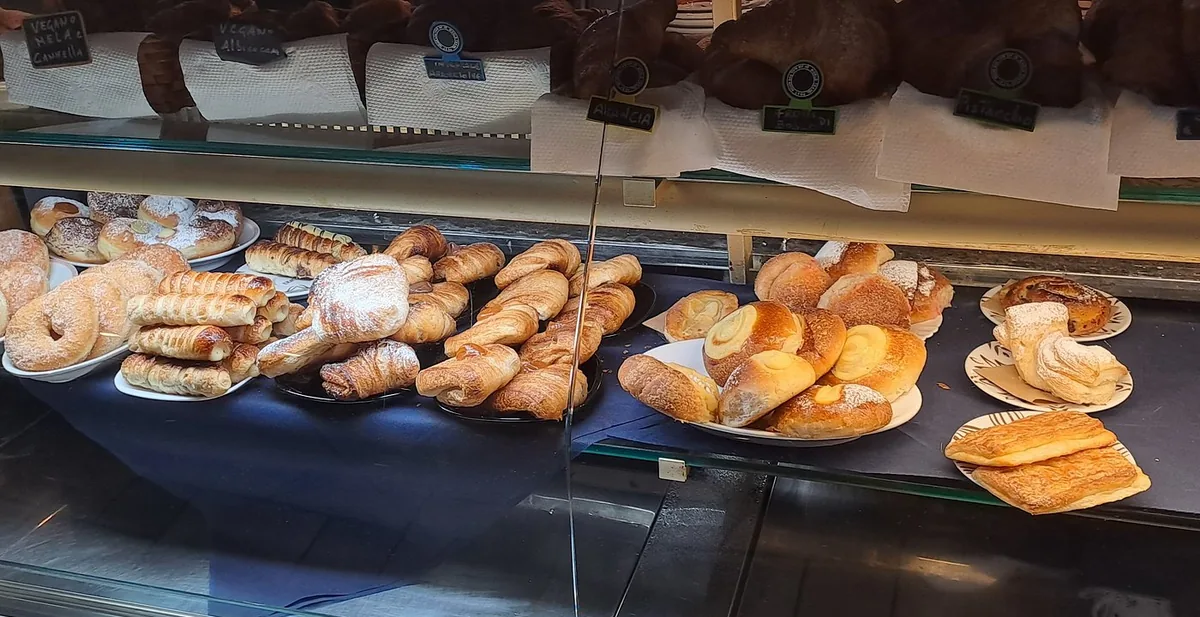 La vetrina delle paste del City Bar: cornetti, sfoglie e ciambelle su vassoi, e sopra i vassoi le lavagnette nere scritte col gesso con i gusti dei ripieni